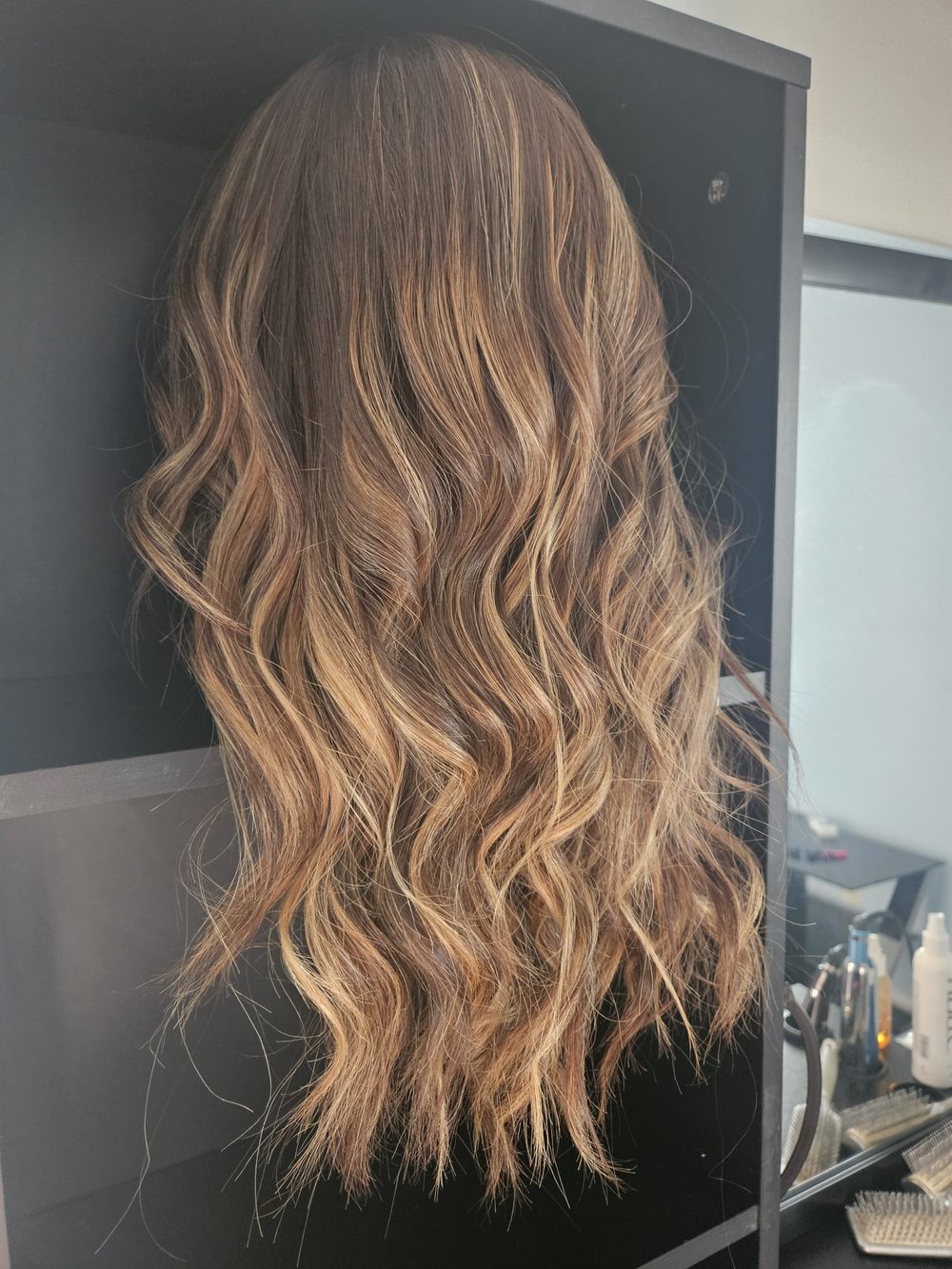 Side view of a long, brunette wig cut and styled by Addi.